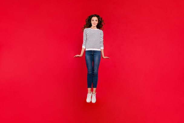 Full length size body photo of attractive she her girl with amazing wave hair jump in air wearing white casual sweater denim jeans isolated on red vivid bright background - Fotoğraf, Görsel