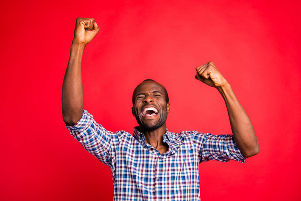 Portrait of nice handsome attractive cheerful glad positive guy wearing checked shirt showing breakthrough gesture holding fists raising hands up isolated over bright vivid shine red background - Foto, imagen