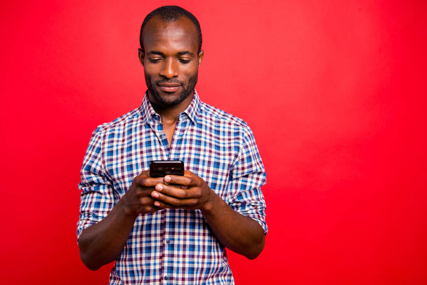 Portrait of he nice handsome attractive cheerful guy wearing checkered shirt holding in hands cell playing game isolated over bright vivid shine red background - Photo, image