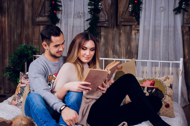 Spending nice time at home. Beautiful young loving couple bonding to each other and smiling while woman holding a book. - Foto, Bild