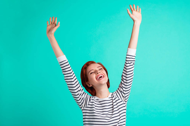 Portrait of her she lovely attractive pretty cheerful optimistic red-haired lady in striped pullover raising hands up having fun isolated over bright vivid shine green turquoise background - Fotoğraf, Görsel