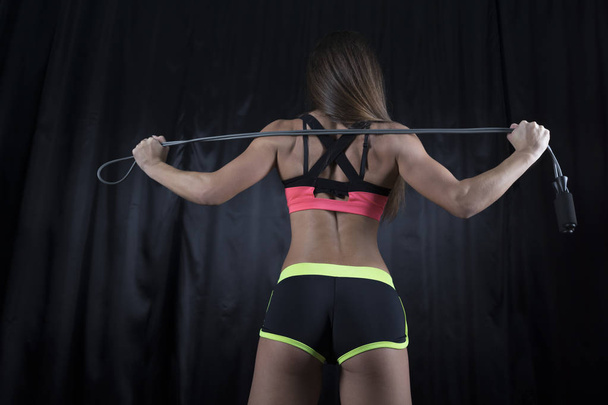Fitness-malli ylä- ja lyhyissä shortseissa, joissa on täydellinen kuva, seisoo taaksepäin kameraan köydellä
 - Valokuva, kuva