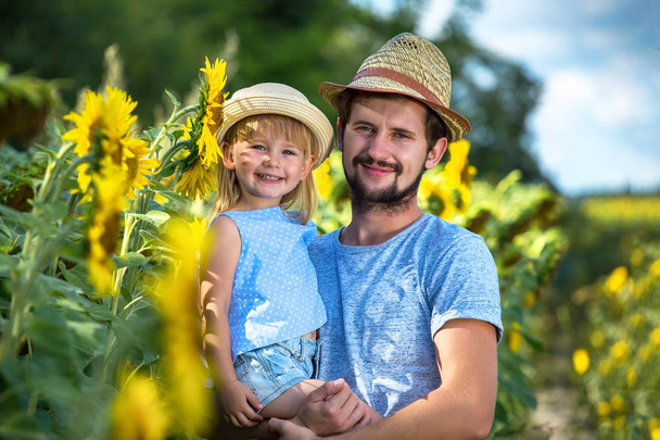 Father and daughter cuddle in the sunflower field. Looking to camera. - Foto, imagen