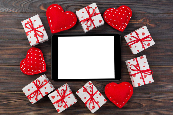 Digital tablet blank screen with gift box and hearts decor on wooden table. Top view. Valentines Day concept background. - Photo, Image