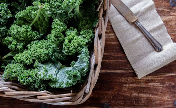 Zelená Kale v košík a nůž na dřevěné pozadí pohled shora na letní superfood zeleninu zátiší - Fotografie, Obrázek