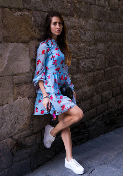 İspanya Tatil serisi. Çiçek seyahat, yaz, tatil, gençlik, güzellik konuda Barcelona'da tuğla duvarın yanında baskı ile mavi elbiseli Genç kız. - Fotoğraf, Görsel