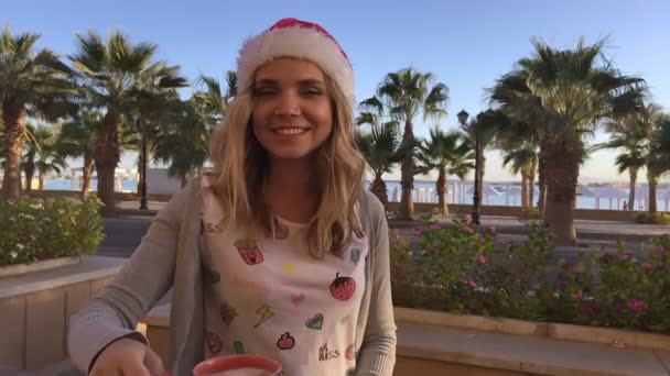 Portret młodej i pięknej kobiety w Boże Narodzenie kapelusz w café palmy i morze - Materiał filmowy, wideo