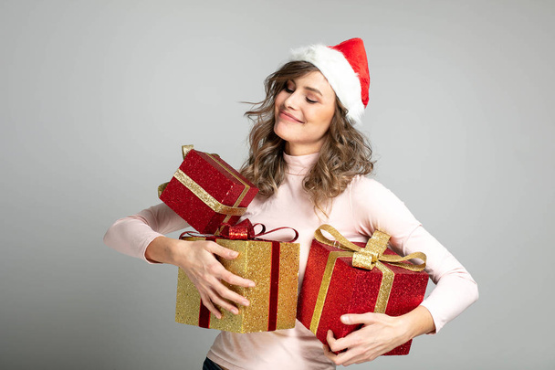 very happy woman with christmas hat holding many gifts in hands - Fotó, kép