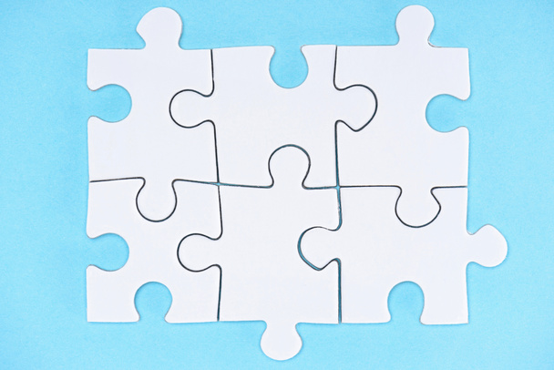 Draufsicht auf arrangierte weiße Puzzle-Elemente auf blauem Hintergrund - Foto, Bild