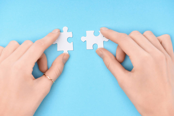 cropped shot of woman holding white puzzles pieces on blue background - Фото, изображение