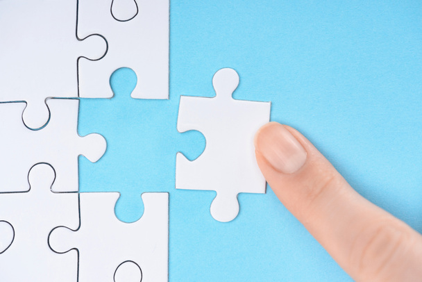 cropped shot of woman pointing at white puzzles pieces on blue background - Photo, Image