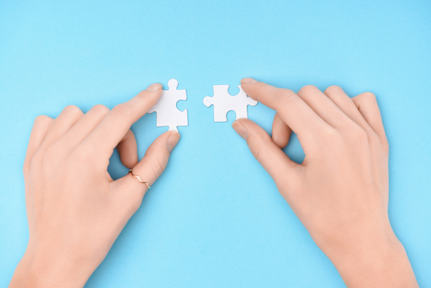 partial view of woman holding white puzzles pieces on blue background - Foto, immagini