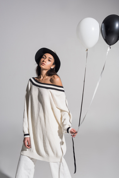 beautiful african american woman in white clothes and hat holding black and white balloons on white - Фото, зображення