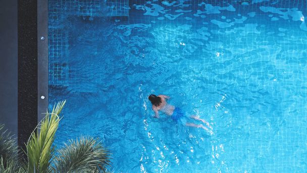 Piscina vista dall'alto angolo che giovane uomo rilassante e godendo nelle piscine del suo hotel nella stagione estiva della Thailandia in giorno di vacanza e hanno luce del sole e bagliori sulla superficie dell'acqua blu. - Foto, immagini
