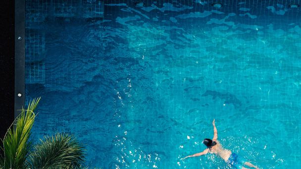 ángulo de vista superior de la piscina que el hombre joven relajarse y disfrutar en las piscinas de su hotel en la temporada de verano de Tailandia en el día de vacaciones y tienen la luz del sol y las bengalas en la superficie de agua azul. - Foto, Imagen