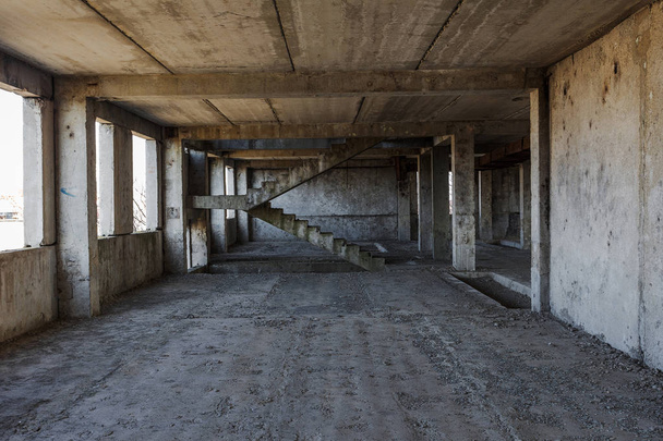 Interieur van een verlaten administratief gebouw. Interieur ruïnes van een industriële fabriek. Een oude betonnen trap, ruïnes, gang met afval en modder, geruïneerd muren van een onafgewerkt office business center, Odessa - Foto, afbeelding