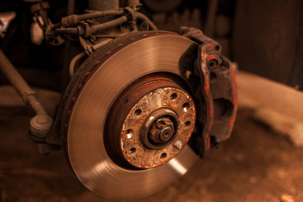 Passenger car with the removal of the wheels is on a hydraulic jack with a naked braking system. Old worn rusty car brake disc with outdated technology. Soft focus, shallow depth of field - Photo, Image