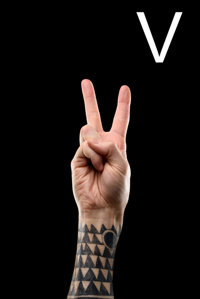 vista parcial de la mano masculina tatuada que muestra la letra latina - V, lenguaje sordo y mudo, aislado en negro
 - Foto, imagen