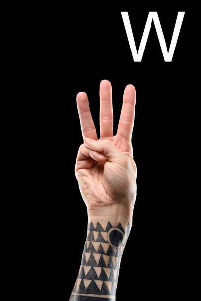 partial view of tattooed male hand showing latin letter - W, deaf and dumb language, isolated on black - Fotó, kép
