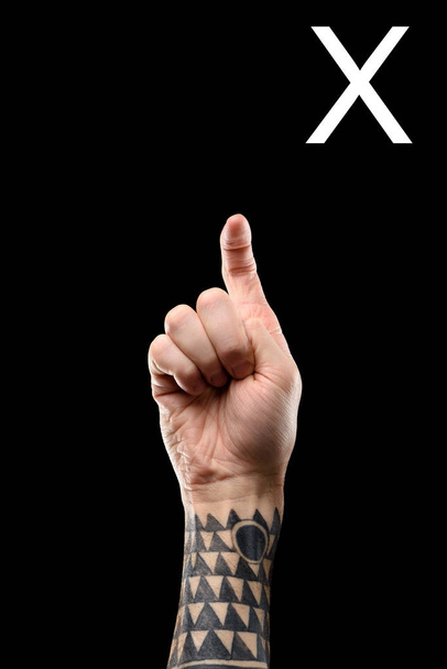 vue partielle de la main masculine tatouée montrant la lettre latine - X, langage sourd et muet, isolé sur noir
 - Photo, image