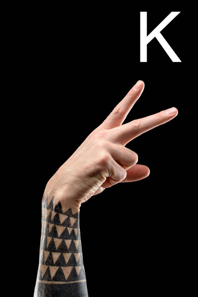 vista parcial de la mano masculina tatuada que muestra letra cirílica, lenguaje sordo y mudo, aislado en negro
 - Foto, Imagen