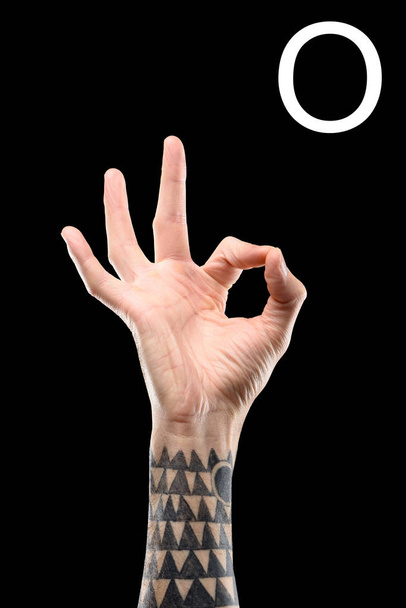 partial view of tattooed male hand showing cyrillic letter, deaf and dumb language, isolated on black - Photo, Image