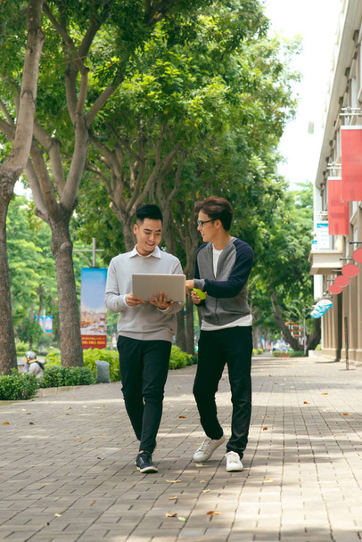 Business colleagues talking while walking on street with laptop - Photo, Image