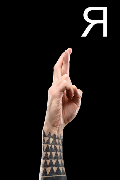 partial view of male tattooed hand showing cyrillic letter, deaf and dumb language, isolated on black - Foto, imagen