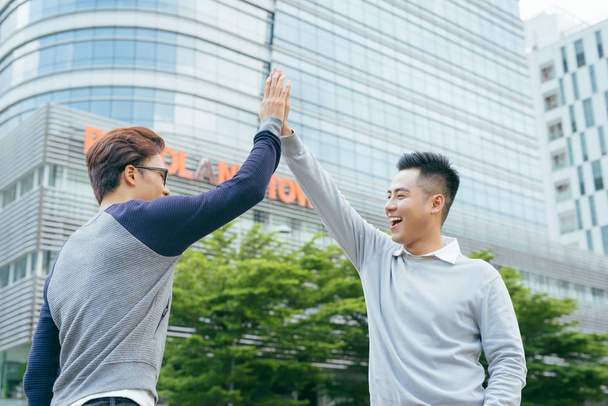 two smiling businessmen giving high five against office building - Photo, Image