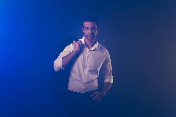 Πορτρέτο του ωραίο δροσερό επιβλητικό αριστοκρατικό κομψή ελκυστική όμορφος άνδρα με αυτοπεποίθηση σε λευκό πουκάμισο κρατώντας σακάκι απομονωμένη φόντο σκούρο μπλε αναθυμιάσεις καπνού - Φωτογραφία, εικόνα