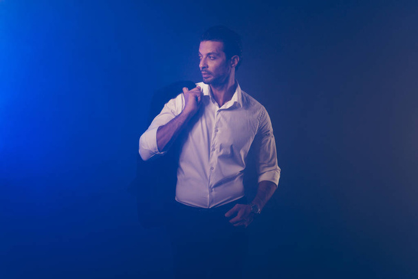Retrato de elegante elegante elegante elegante atractivo atractivo confiado contenido hombre en camisa blanca que sostiene chaqueta mirando a un lado aislado sobre humo azul oscuro fondo
 - Foto, imagen