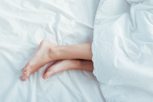Unterteil der weiblichen Beine unter Decke im Bett - Foto, Bild