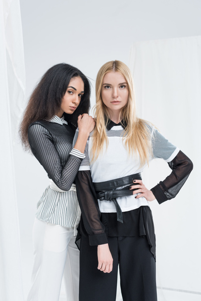 attractive multicultural brunette and blonde women in black and white clothes posing isolated on white - Fotografie, Obrázek