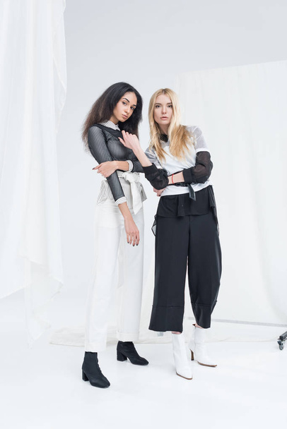 full length of attractive multiethnic women in black and white clothes posing on white - Zdjęcie, obraz
