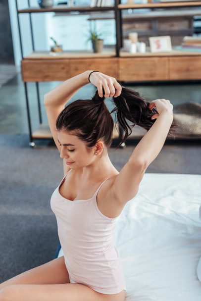 high angle view of girl collecting ponytail while sitting on bed during morning time at home - Photo, Image