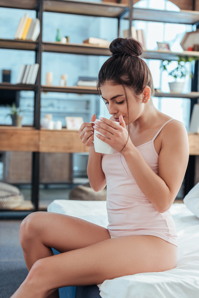 όμορφη νεαρή γυναίκα που πίνει καφέ στο κρεβάτι κατά τη διάρκεια του χρόνου το πρωί στο σπίτι - Φωτογραφία, εικόνα