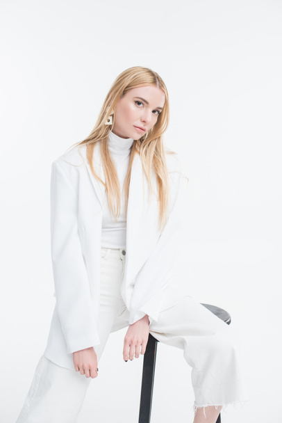 attractive caucasian blonde woman in fashionable white sweater and jacket sitting on chair and looking at camera isolated on white - Photo, Image