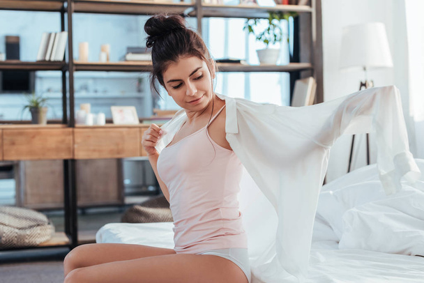 happy young woman putting on white shirt during morning time at home - Foto, Imagem