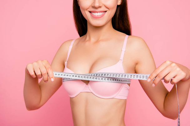 Cropped close-up photo of nice cute adorable attractive cheerful positive optimistic girl in beige bra measuring chest size line with tape isolated over pink background - 写真・画像