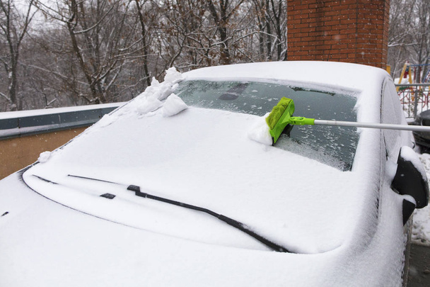 Длинная раскладная зеленая щетка очищает снег от лобового стекла автомобиля
 - Фото, изображение