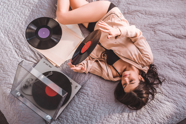 high angle view of woman laying on bed and listening vinyl audio player at home - 写真・画像
