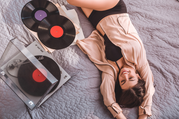 high angle view of girl laying on bed and listening vinyl audio player at home - Photo, Image