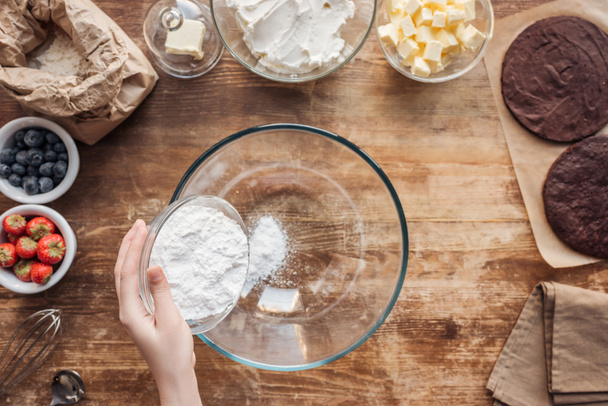 partial top view of woman holding flour and preparing dough for delicious homemade cake - Photo, Image
