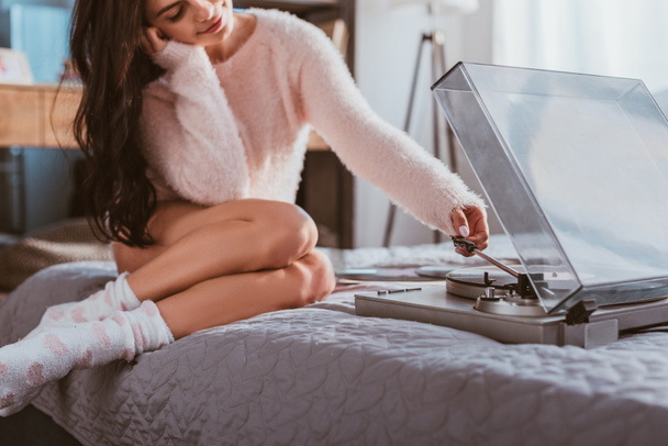 selective focus of girl sitting on bed and turning on vinyl audio player at home - Foto, Imagem