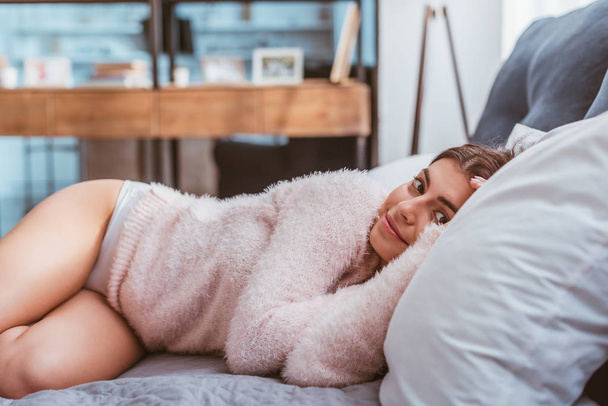 smiling young woman in pink fluffy sweater laying on bed at home - Foto, Imagen