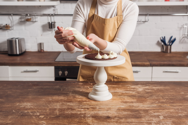 visão parcial da mulher no avental decorando bolo caseiro doce com creme
   - Foto, Imagem