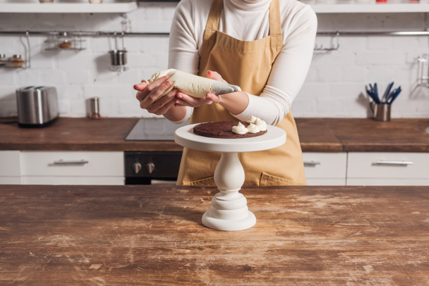 cropped shot of woman in apron decorating sweet homemade cake with cream  - Photo, Image