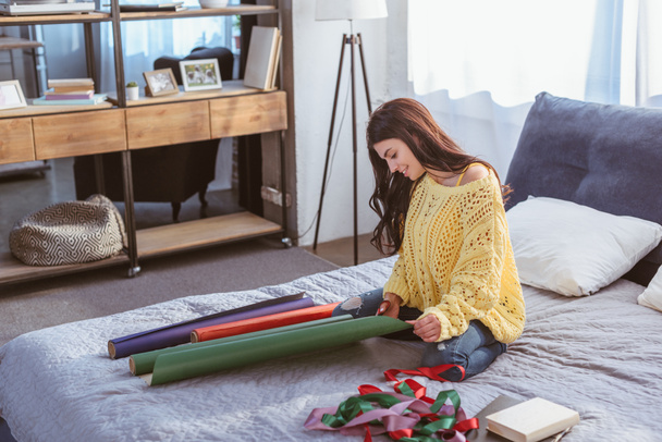 smiling girl packing christmas gift while sitting on bed at home - 写真・画像