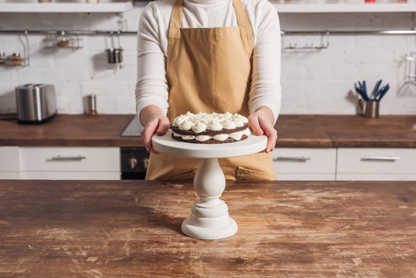 abgeschnittene Aufnahme einer Frau in Schürze, die köstlichen süßen Kuchen mit Sahne kocht  - Foto, Bild