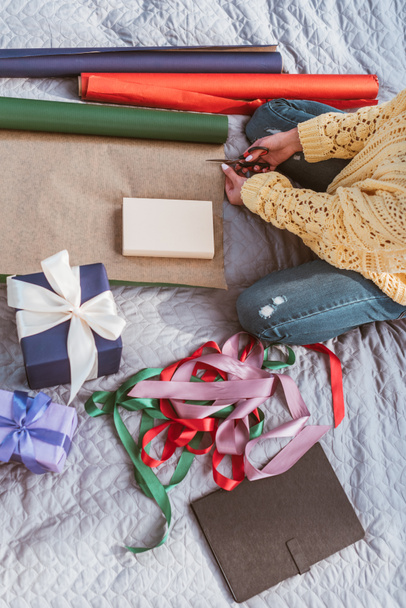 abgeschnittenes Bild einer jungen Frau beim Verpacken von Geschenken, während sie zu Hause auf dem Bett sitzt - Foto, Bild